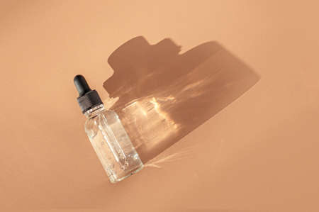 Transparent glass dropper bottle with air bubbles on beige background in sunlight. Pipette with fluid hyaluronic acid, serum, retinol. Cosmetics and healthcare concept Flat lay. Luxury beauty productの写真素材