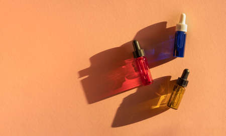Transparent glass dropper bottles with green, red and blue liquid inside on beige background in the...