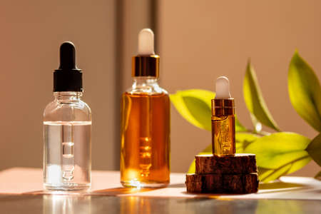 Three cosmetic glass dropper bottles with serum, oil or peeling in sunlight with green flower...