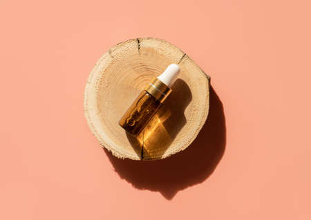 Amber glass dropper bottle on woodcut in the sunlight with eucalyptus flower shadows. Top view. Luxury and natural cosmetics presentation. Testers, beauty samples perfumery concept. Shades and lightsの写真素材