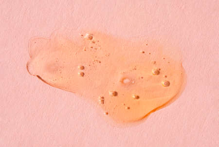 Orange cosmetics gel, serum or peeling drop on pink background. Colorful warm yellow slime with air bubbles in the sunlight. High contrast trendy photo. Health protection and self-care conceptの写真素材