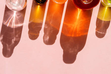 Different cosmetic glass bottles standing on pink background. Abstract pattern by shadows and illuminating reflections in the sunlight. Red, green and yellow shades. Flat lay style with copy spaceの写真素材