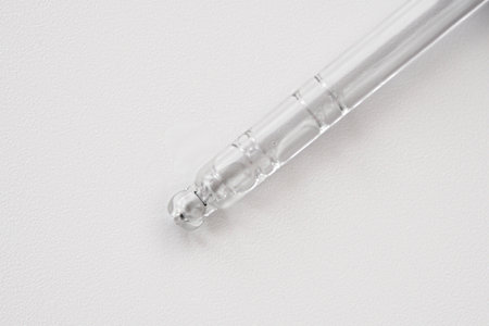 Pipette with fluid hyaluronic acid on blue background. Cosmetics and healthcare concept closeup....