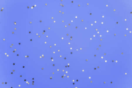 Silver stars glittering confetti on blue background. Trendy festive holiday backdrop. Many...