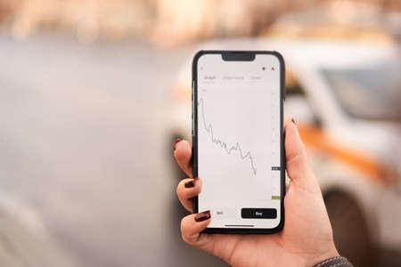 Female hand holding a mobile phone with graph doing down - stock market concept. Template for web...