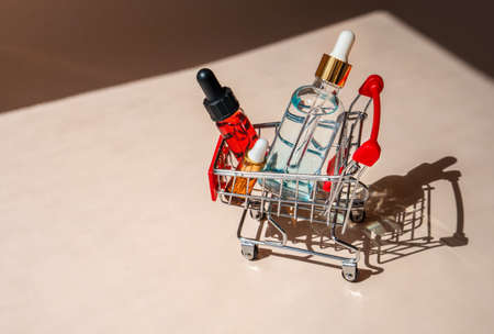 Online shopping minimalistic concept. Small cart with cosmetic bottles. Essential oil, serum and...
