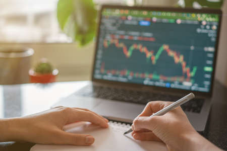 Female hands writing down numbers from laptop. Investment analysis, trading concept. Technology,...