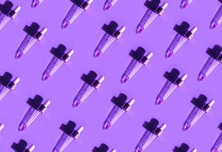 Pipette with gold metallic cap and drops of water, serum, oil, beauty product on violet background. Natural medicine, cosmetic research, bio science. Concept of skincare, analysis. Flat lay, patternの写真素材