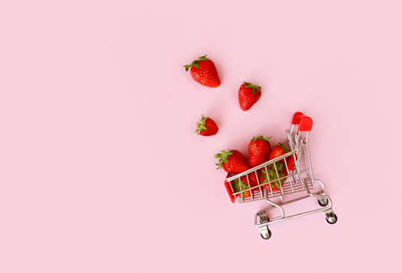 Fresh red strawberry in shopping cart on pink background. Online shopping and Valentines Day minimalistic concept. Black Fridays sales banner. Healthy, organic, vegan foodの写真素材