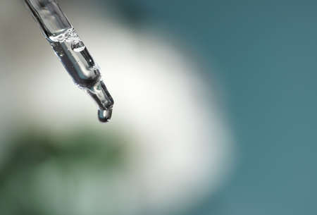 Pipette with transparent fluid hyaluronic acid or serum. Cosmetics, science and healthcare concept closeup. Dose of serum or retinol falls in a bottle. Front view. Beauty product presentation, macroの写真素材