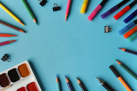 Stationary supplies on blue background framing space for text. Office accessories flat lay. The first September, back to school, education, creativity concept. Pens, pencils and paints with copyspaceの写真素材