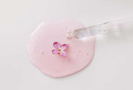Closeup of pipette with serum, oil, gel with lilac flowers on white background. Skin care, natural...