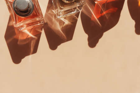 Different glass perfume bottles in row making pattern by luminous shadows and lights standing on trendy beige background. Abstract pattern by shadows and illuminating reflections in the sunlight.の写真素材