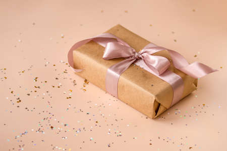 Valentines Day, Birthday or New Year present in kraft paper with pink ribbon on soft beige...