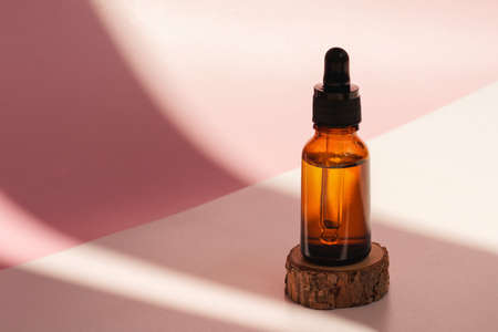 Cosmetic amber glass dropper bottle on wooden podium with oil, serum or fruit peeling in the sunlight. Beauty product presentation, natural pink background. Front view. Mockup conceptの写真素材