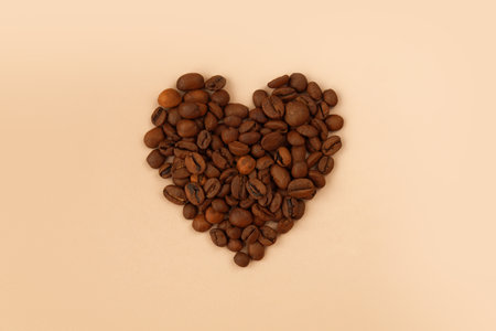 Heart made of coffee beans on pastel beige background. Freshly roasted beans flat lay. Symbol of love, breakfast time and morning routine.の写真素材