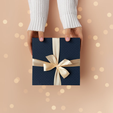 Christmas background. Female hands in white sweater with natural manicure hold blue gift box with gold ribbon. Xmas and New Year postcard design. Black Friday sales, Birthday celebration party conceptの写真素材