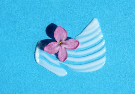 Texture of white cream with lilac flower on blue background. Smear of moisturizer closeup. Lotion swatch. Beauty, skin care product smear smudge drop. SPF sunscreen cream sampleの写真素材