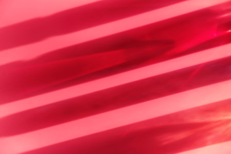 Different cosmetic glass bottles standing on pink background. Abstract beauty pattern by shadows and reflections in the sunlight. Red, green and yellow shades. Flat lay style with copy spaceの写真素材