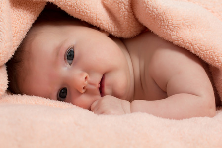 Baby girl is hiding under the peach-coloured blanketの写真素材