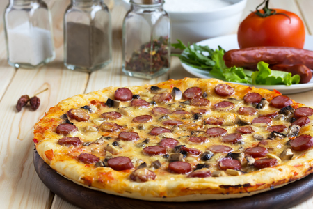 Homemade Pizza with hunter sausages and mushrooms on wooden table backgroundの写真素材