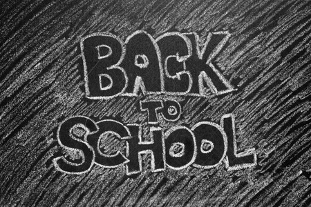 Black and white image of back to school phrase written on blackboard background for your design