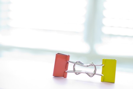 Colorful binder clip on white table near white window. long-tail clip, one kind of stationery.