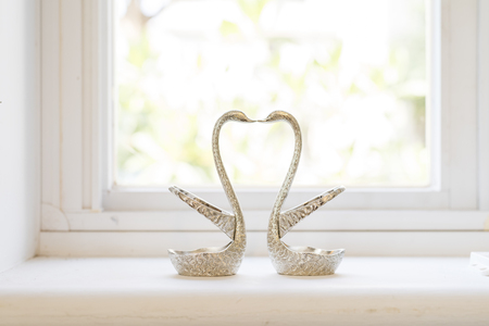 Glossy Silver Metallic Swan Decoration Kissing on Top of White Table near the Glass Window.の写真素材