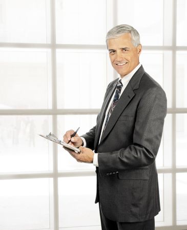 Mature businessman with clipboard in office next to wall of windowsの写真素材