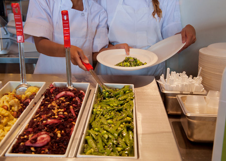 Food in trays and workers hands serving. の写真素材