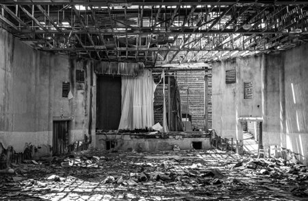 Black and White Monochrome Abandoned and Decaying Building with a Movie Theater Screen with trash on the floor and sunlight beams through exposed skyの写真素材