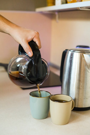 Man pouring hot coffee from teapot into cups on kitchen counterの写真素材