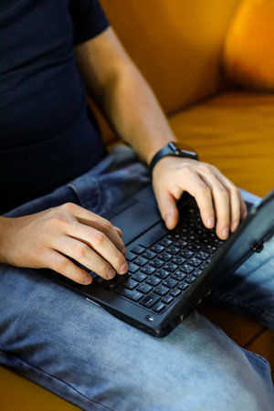 Close-up of male hands typing on laptop keyboard on sofa at homeの写真素材