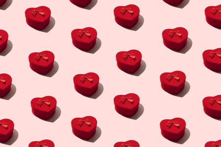 A heart shaped red box with ribbon on a pink pastel background. Pattern.