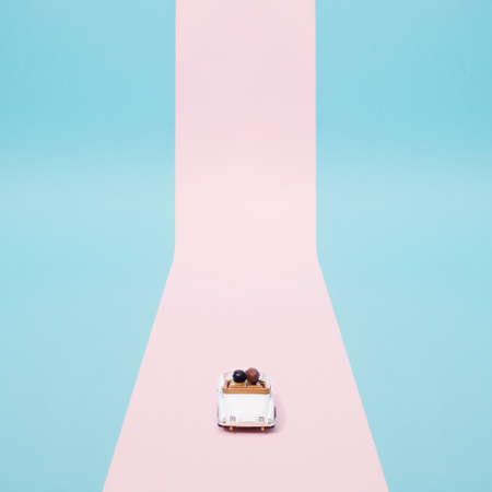 Two plastic toy figures. Man and wife in a classic white limousine. Blue and pink background....