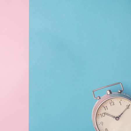 Metal old clock in corner on blue and pink background. Copy space. Minimal concept.の写真素材