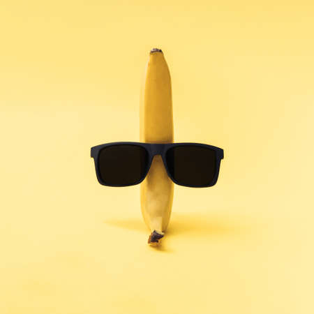 Yellow banana with black sunglasses. Yellow background. Minimal composition.の写真素材