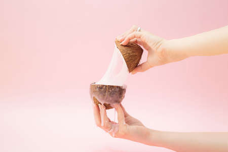 A beautiful female hand holding coconut from which a slime comes out. Pink background.の写真素材