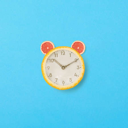 An old clock in orange with grapefruit.. Minimal design on blue background.  The bell on the clock...