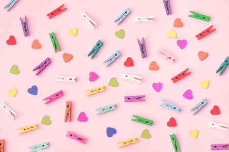 Small colorful wooden laundry tongs with colorful wooden hearts arranged on a pink background.の写真素材
