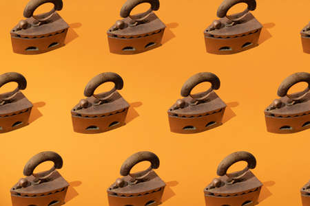 Rusty old metal steam iron on orange background. Minimal design and pattern.の写真素材