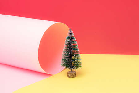New year snowy tree stand on a yellow paper with pink tube 
roll and red pastel background. Christmas scene. Minimal design. Copy space.の写真素材