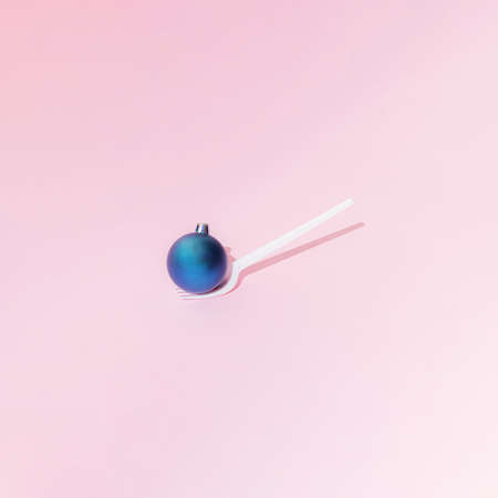 A Christmas and New Year blue bauble  stands on a white plastic fork on a pink background. Minimal design. Copy space.の写真素材
