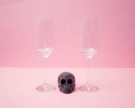 Two empty glasses of champagne with a skeleton head between them. Dark black gray candle skull. Minimal conceptの写真素材