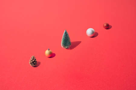 Arranged New Year and Christmas tree with yellow gold, silver, red  bauble and brown pinecone on a red pastel background. Pattern.の写真素材