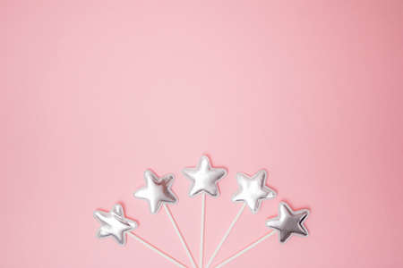 Arranged five silver gummy toy star on a stick. Pink background. Minimal design. Copy space. Flat...