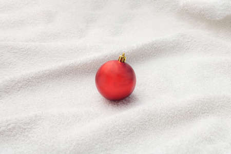 Red new year Christmas bauble with golden head on white snowy towel. Pastel colors. Minimal design....