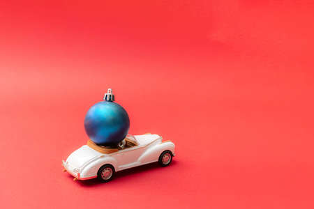 Christmas blue bauble on a luxury white cabriolet limousine. Red pastel background. Minimal new year design.の写真素材