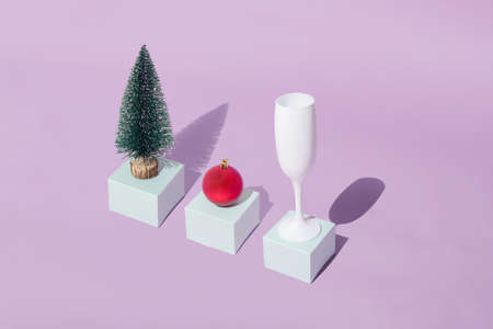 Arranged new year christmas tree with red bauble and white champagne glass on turquoise cardboard gift box on purple pastel background.の写真素材