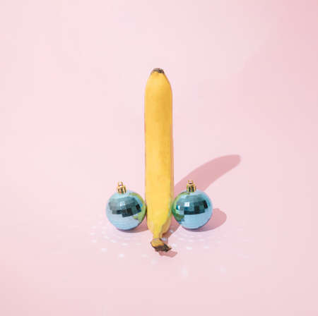 Yellow banana with two light blue party disco ball on pink pastel background. Minimal holiday...